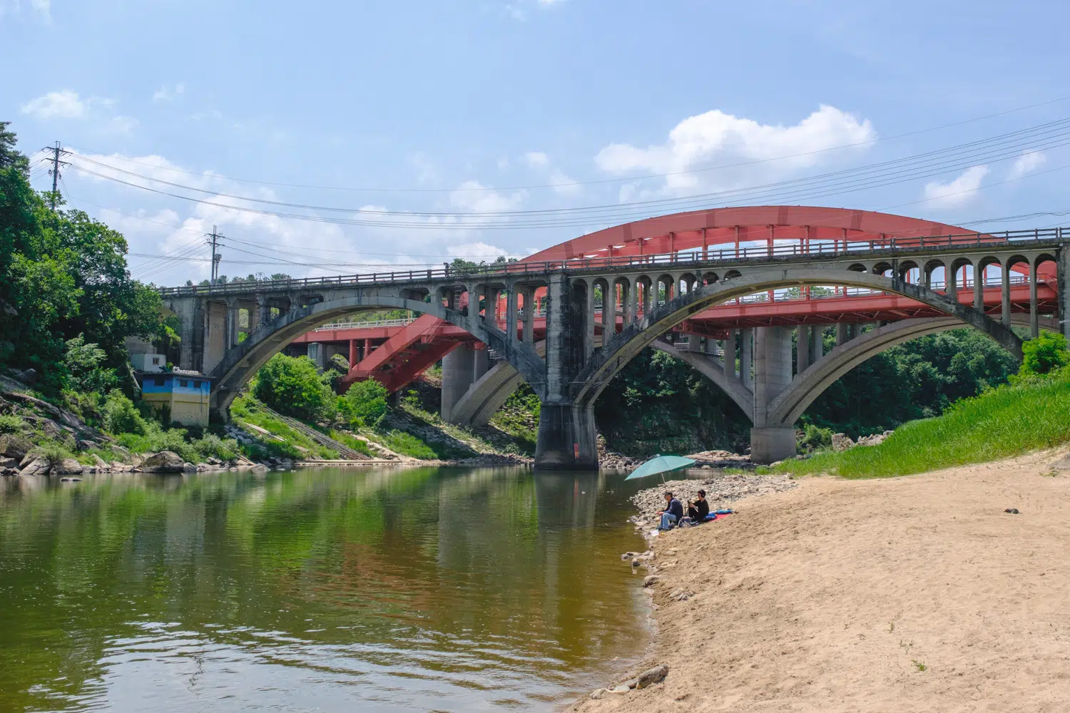 cheorwon-hantan-river-bridge-seungilgyo-2025 A couple of anglers sits underneath an umbrella near the Seungilgyo bridge over the Hantan River in Cheorwon (June 2025).
