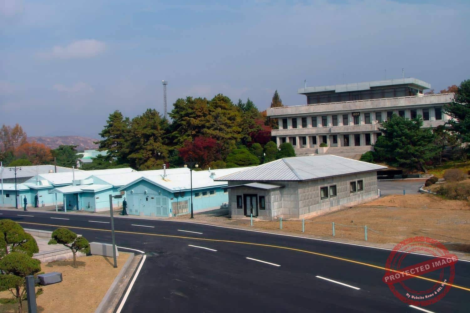 jsa-panmunjom-200511-10 The huts formerly used for cross-border negotiations, which straddle the military demarcation line (indicated by a change in grass color). At the rear, the Panmungak, the official North Korean building (November 2005).