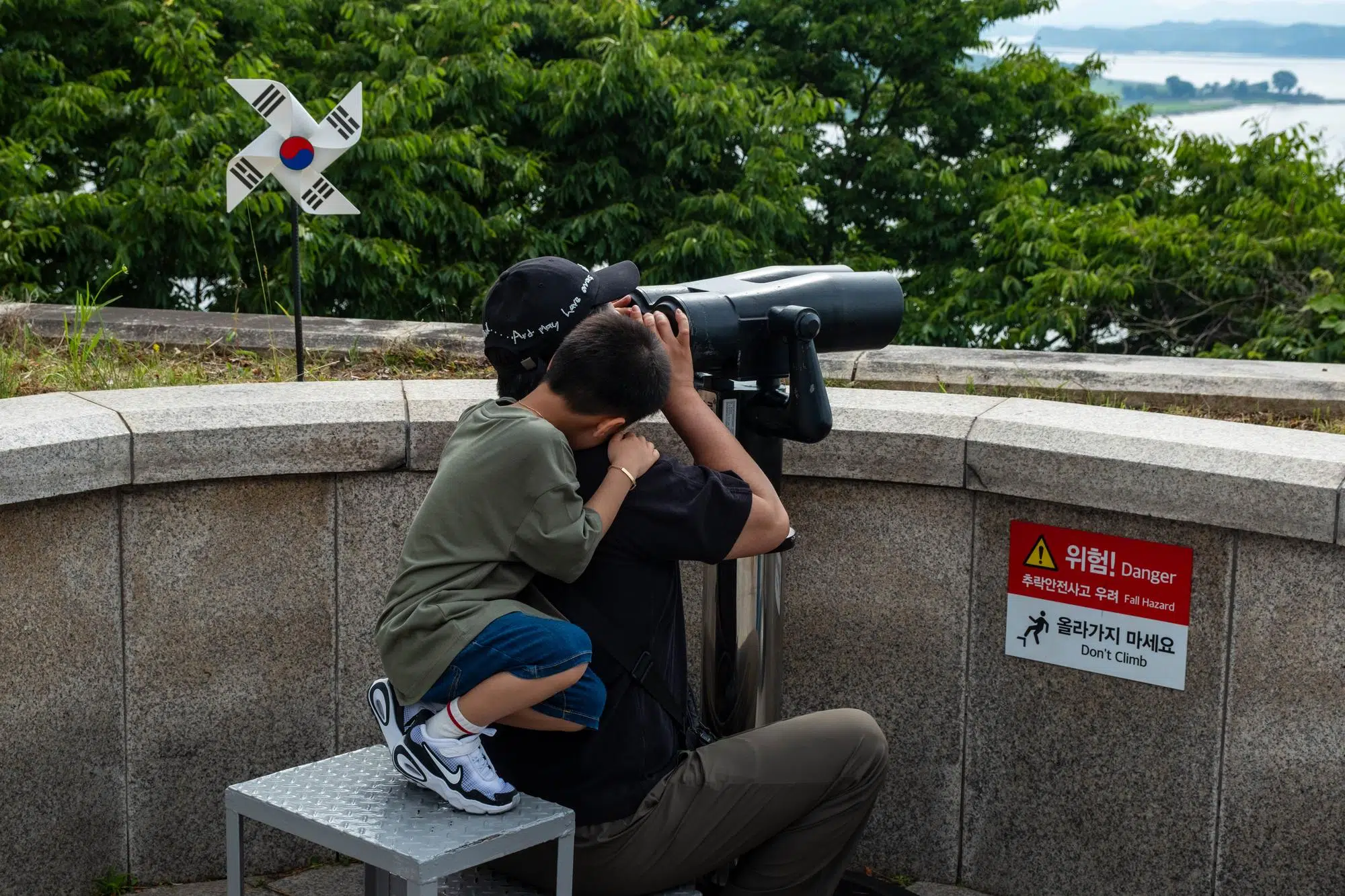 odusan-observatory-june-2026-1 A boy grabs his fathers while he watches North Korea through a telescope from Odusan Observatory in Paju.